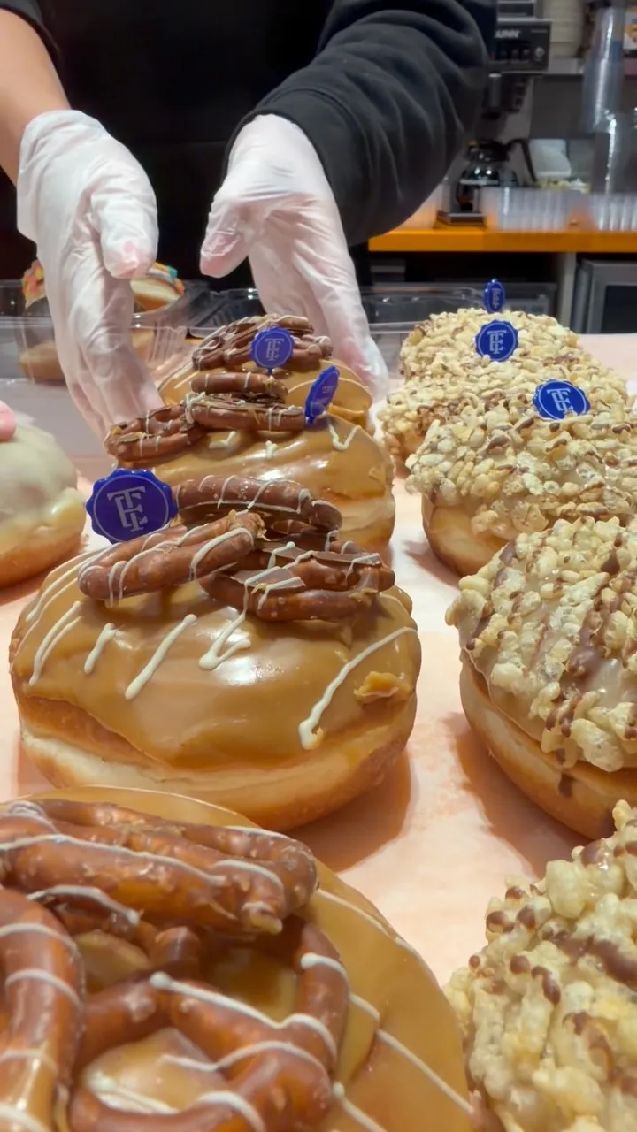 Caramel pretzel donuts being topped, each with a Taam Eden seal